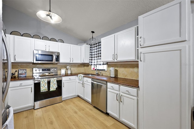 kitchen with dark countertops, light wood-style floors, appliances with stainless steel finishes, white cabinets, and vaulted ceiling