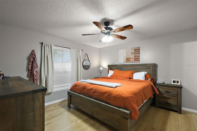 bedroom featuring ceiling fan, baseboards, a textured ceiling, and light wood-style flooring