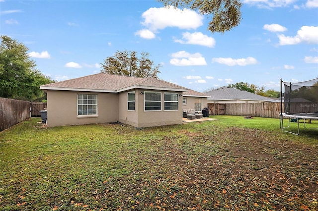 rear view of property with a trampoline, a fenced backyard, a yard, and stucco siding