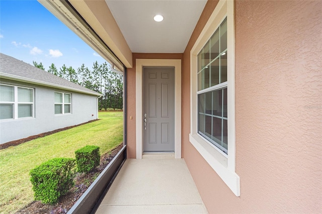 view of exterior entry with stucco siding and a lawn