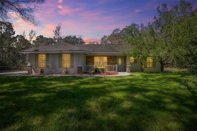 back of house at dusk featuring stucco siding, stone siding, a lawn, and covered porch