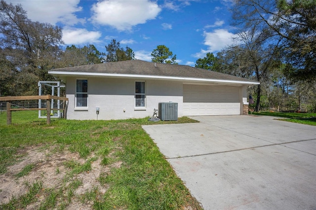 back of property with central AC unit, an attached garage, stucco siding, concrete driveway, and a lawn