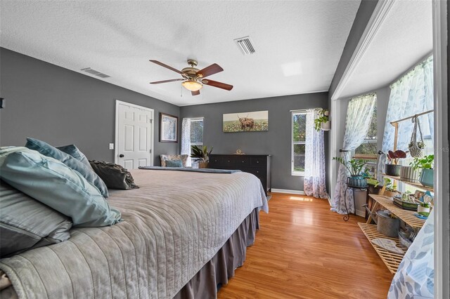 bedroom with visible vents, a textured ceiling, light wood-style floors, and a ceiling fan