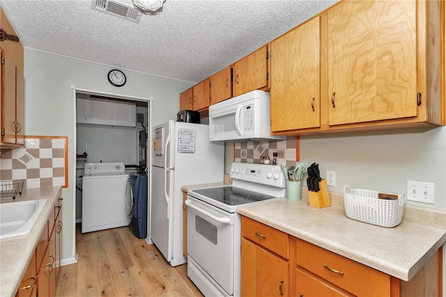 kitchen featuring visible vents, light wood-style flooring, a sink, white appliances, and light countertops