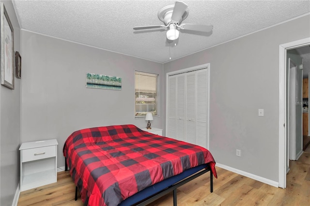 bedroom with ceiling fan, baseboards, light wood-type flooring, a closet, and a textured ceiling