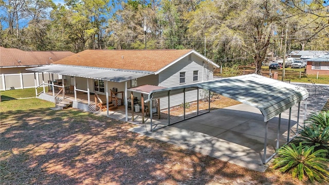 rear view of property featuring a shingled roof, concrete driveway, a yard, and fence