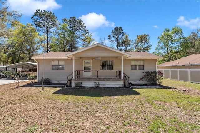 view of front of property featuring a front yard, fence, covered porch, a shingled roof, and a carport