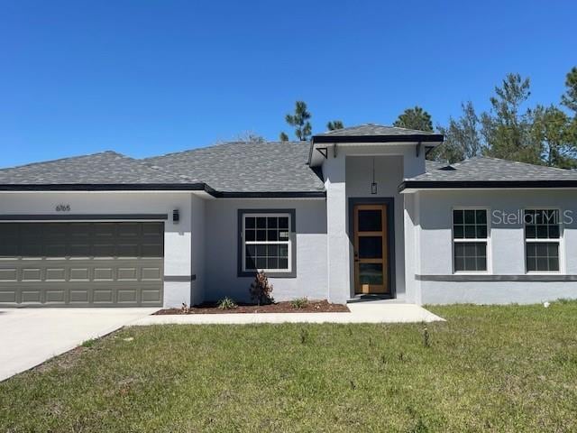 view of front facade with stucco siding, driveway, a front yard, a shingled roof, and a garage