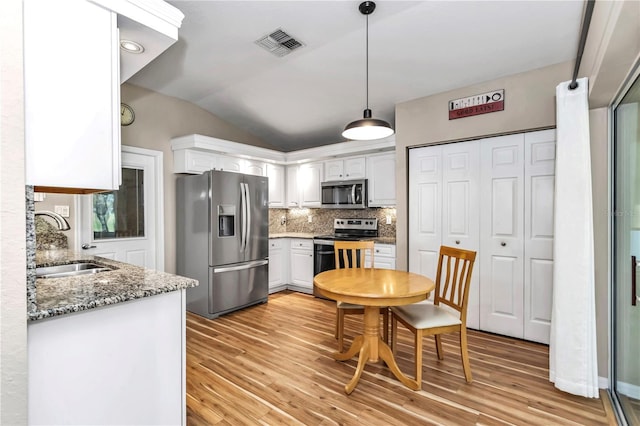 kitchen featuring visible vents, lofted ceiling, a sink, stainless steel appliances, and white cabinetry