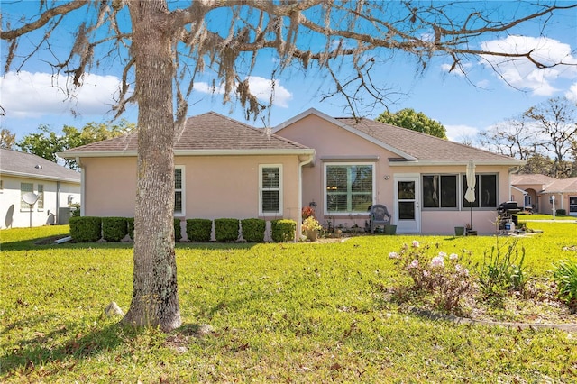 back of property with central air condition unit, stucco siding, a lawn, and a shingled roof