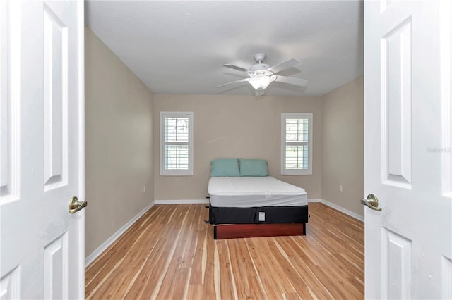 unfurnished bedroom with baseboards, multiple windows, a ceiling fan, and light wood finished floors