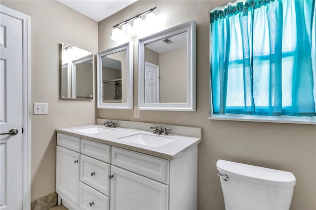 full bath with a sink, visible vents, toilet, and double vanity