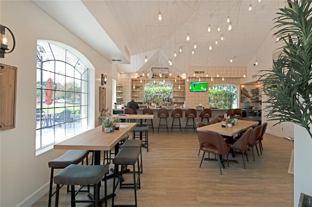 dining space featuring built in features, wood finished floors, visible vents, baseboards, and vaulted ceiling