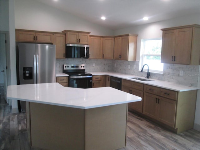 kitchen with wood finished floors, appliances with stainless steel finishes, lofted ceiling, a sink, and a center island