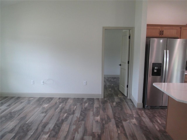 kitchen featuring light countertops, stainless steel fridge, dark wood finished floors, brown cabinetry, and baseboards