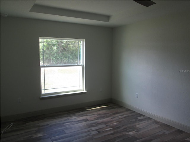 unfurnished room featuring baseboards, dark wood-style flooring, and a raised ceiling