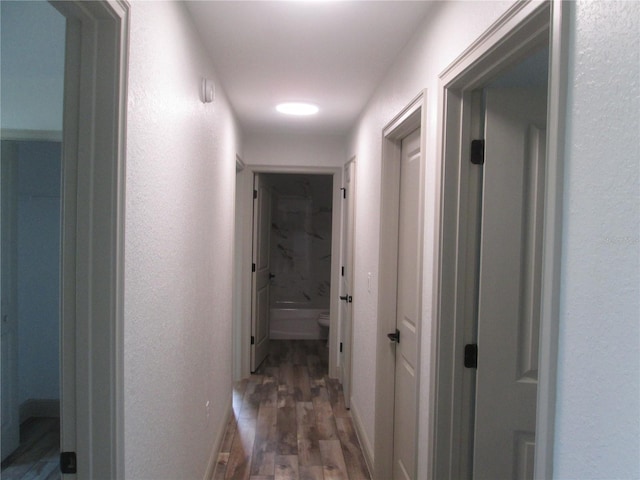 corridor with a textured wall, baseboards, and wood finished floors