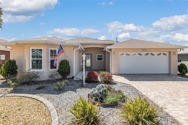 view of front of home with decorative driveway, an attached garage, roof with shingles, and stucco siding