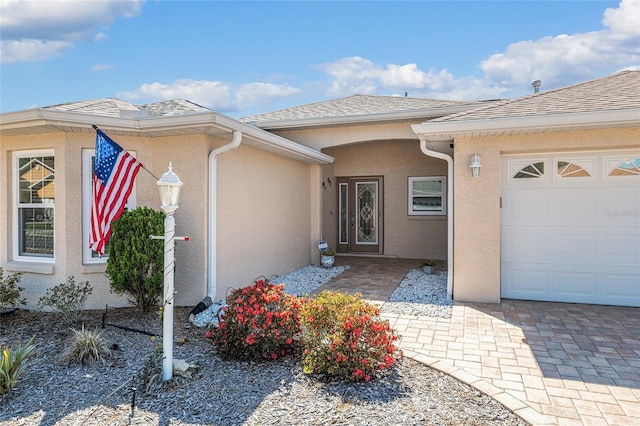 property entrance with stucco siding, an attached garage, and roof with shingles