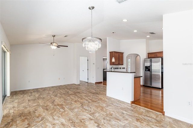 kitchen with brown cabinets, arched walkways, stainless steel fridge, dark countertops, and open floor plan