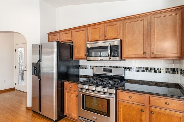 kitchen with arched walkways, brown cabinets, appliances with stainless steel finishes, and tasteful backsplash