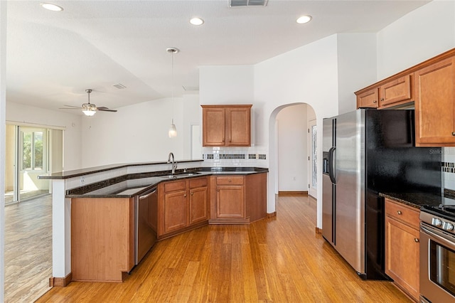 kitchen with brown cabinetry, a peninsula, arched walkways, a sink, and appliances with stainless steel finishes