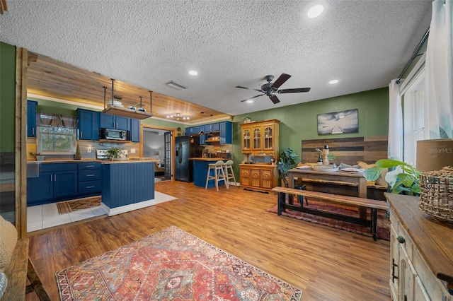 kitchen with stainless steel microwave, visible vents, wooden counters, black refrigerator with ice dispenser, and blue cabinets