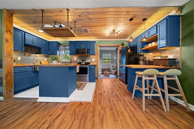 kitchen featuring a breakfast bar area, blue cabinetry, stainless steel electric range, freestanding refrigerator, and butcher block countertops