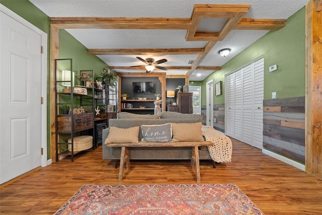 living room featuring beam ceiling, a textured ceiling, wood finished floors, attic access, and ceiling fan