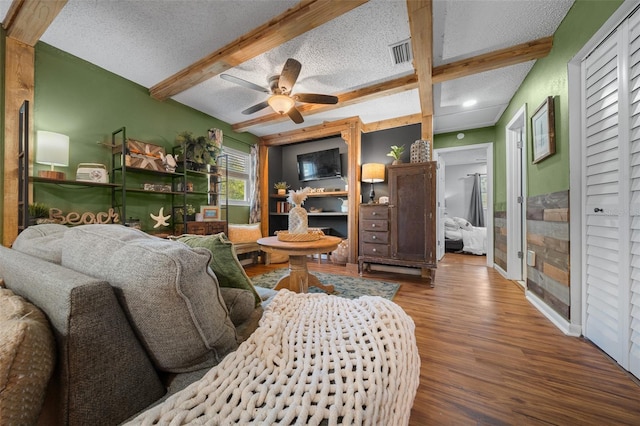 living room featuring visible vents, a textured ceiling, beamed ceiling, and wood finished floors