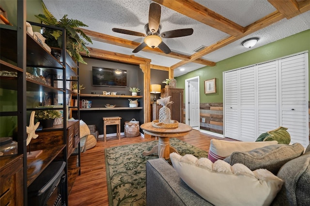 living area with beamed ceiling, a textured ceiling, coffered ceiling, wood finished floors, and ceiling fan