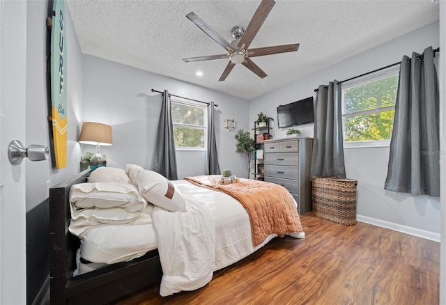 bedroom with multiple windows, wood finished floors, baseboards, and a textured ceiling