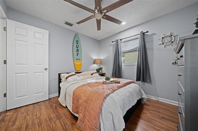 bedroom with a ceiling fan, baseboards, wood finished floors, visible vents, and a textured ceiling