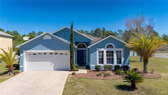 ranch-style home featuring decorative driveway, a garage, a front lawn, and stucco siding