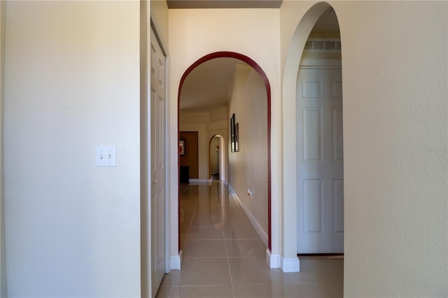 corridor featuring arched walkways, light tile patterned floors, baseboards, and visible vents