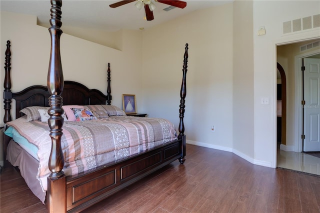 bedroom with arched walkways, wood finished floors, visible vents, and baseboards