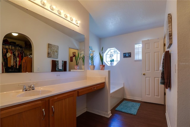 bathroom with a bath, a spacious closet, vanity, and wood finished floors