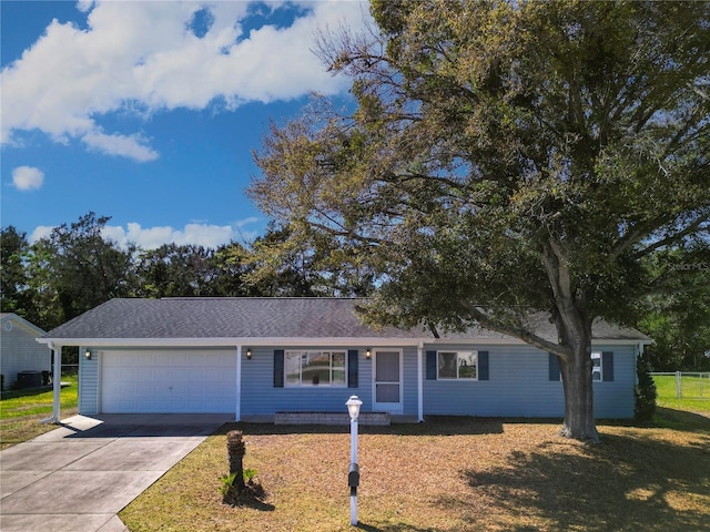 ranch-style house with an attached garage, concrete driveway, a front lawn, and roof with shingles