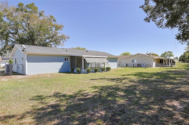 rear view of property featuring a sunroom, a lawn, and fence