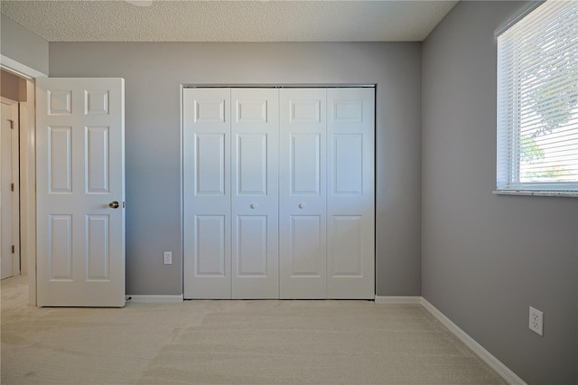 unfurnished bedroom with light carpet, a textured ceiling, baseboards, and a closet
