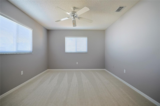 empty room featuring baseboards, visible vents, ceiling fan, a textured ceiling, and light colored carpet