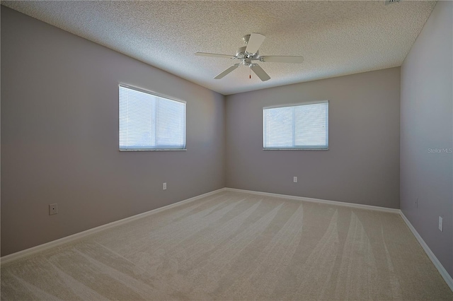 empty room featuring a textured ceiling, a ceiling fan, baseboards, and light carpet