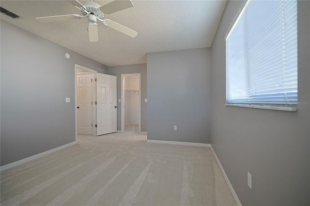 empty room with visible vents, light colored carpet, a textured ceiling, and baseboards