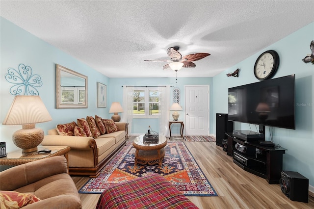 living area featuring baseboards, a textured ceiling, light wood-type flooring, and a ceiling fan