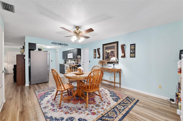 dining space with visible vents, baseboards, light wood-type flooring, a textured ceiling, and a ceiling fan