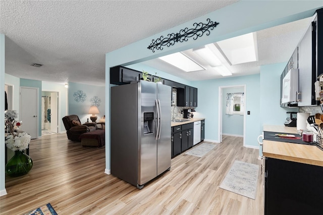 kitchen featuring dark cabinets, visible vents, appliances with stainless steel finishes, and light wood-type flooring