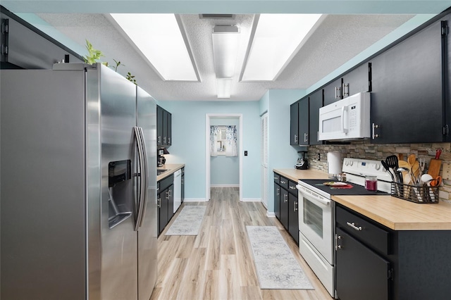 kitchen featuring backsplash, a textured ceiling, white appliances, light wood-style floors, and dark cabinets