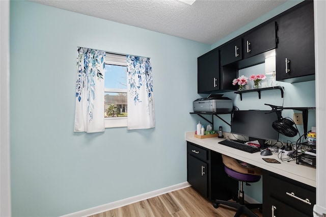 office area featuring baseboards, a textured ceiling, and light wood finished floors