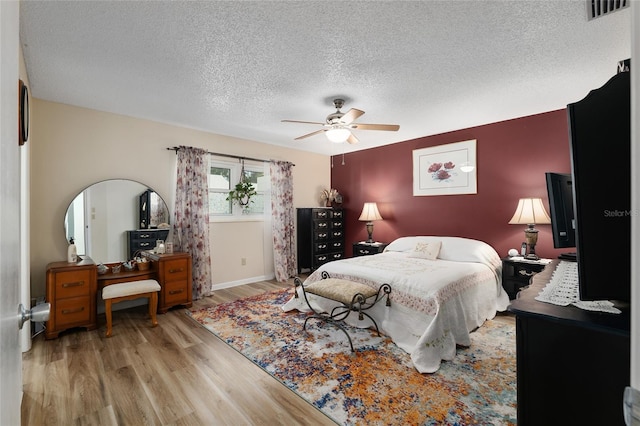 bedroom with wood finished floors, baseboards, visible vents, ceiling fan, and a textured ceiling