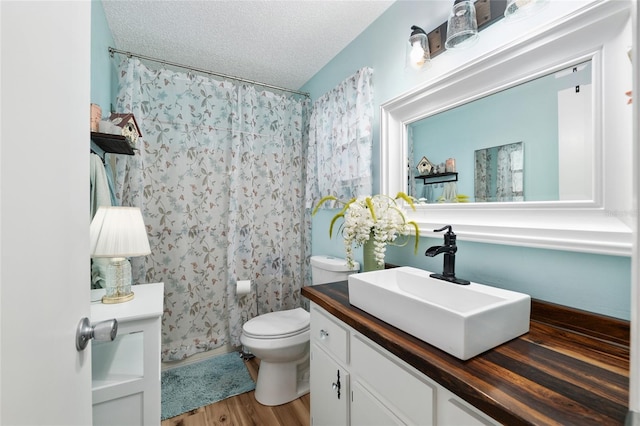 full bathroom featuring toilet, a textured ceiling, vanity, and wood finished floors